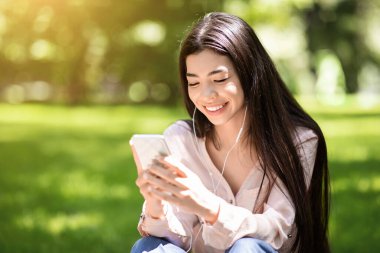 En sevdiği eğlence yeri. Akıllı telefon ve kulaklıklarla dışarıda müzik dinleyen mutlu Asyalı kız.