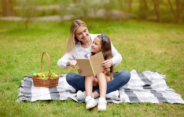 Mor och dotter läser bok under sommaren picknick i parken — Stockfoto