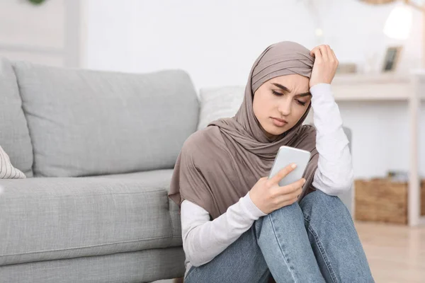 Unangenehme Botschaft. Depressives arabisches Mädchen sitzt zu Hause und schaut auf Smartphone-Bildschirm — Stockfoto