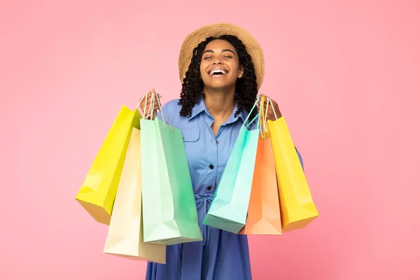 Chica negra riendo llevando bolsas de compras de pie sobre fondo rosa —  Fotos de Stock