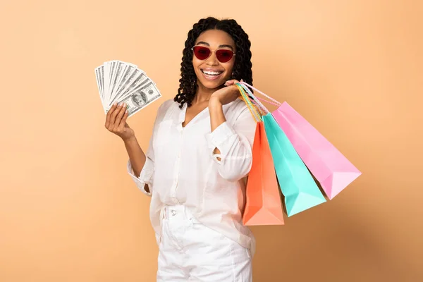Šťastná africká dívka drží peníze a nákupní tašky, béžové pozadí — Stock fotografie