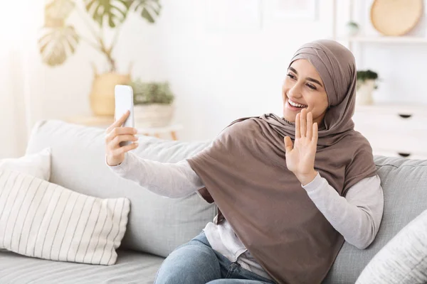 Video panggilan. Muslim gadis di hijab melambaikan tangan ke kamera smartphone di rumah — Stok Foto