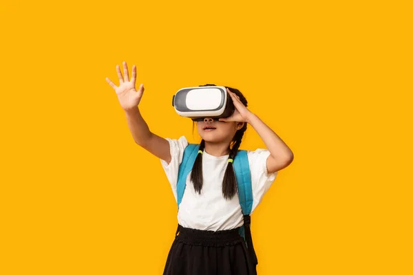 Asiatiska skolflicka bär Virtual Reality glasögon stående över gul bakgrund — Stockfoto