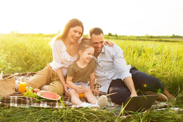 Familia feliz juntos en un picnic con computadora personal — Foto de Stock