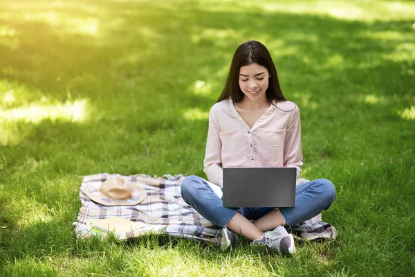 Estudiante coreana chica estudiando al aire libre con el ordenador portátil en el parque, sentado en el césped —  Fotos de Stock