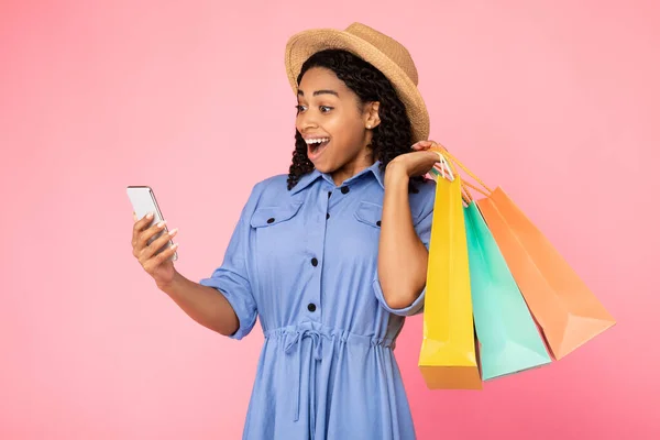 Donna eccitata che tiene il cellulare in piedi con borse shopper, sfondo rosa — Foto Stock