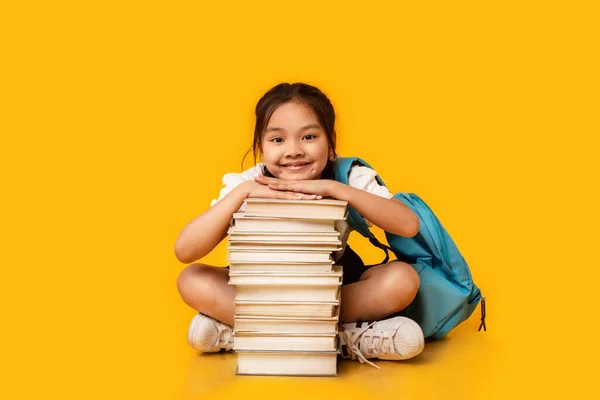 Ασιατική μαθήτρια κάθεται σε στοίβα βιβλίο σχετικά με κίτρινο φόντο στούντιο — Φωτογραφία Αρχείου