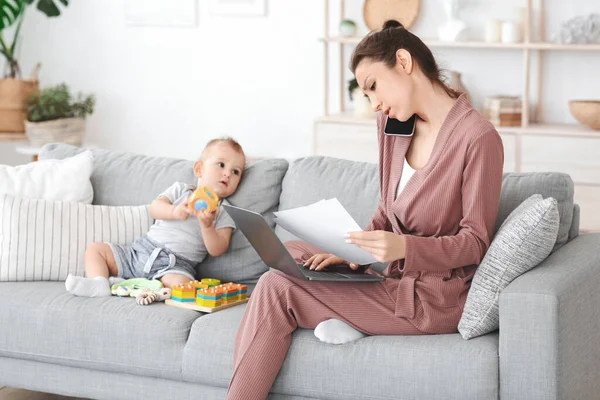 Mère travaillant à la maison avec un ordinateur portable et des papiers à côté de son bébé — Photo
