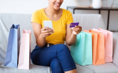 Evde telefon ve kredi kartı kullanan siyah bir kadın.