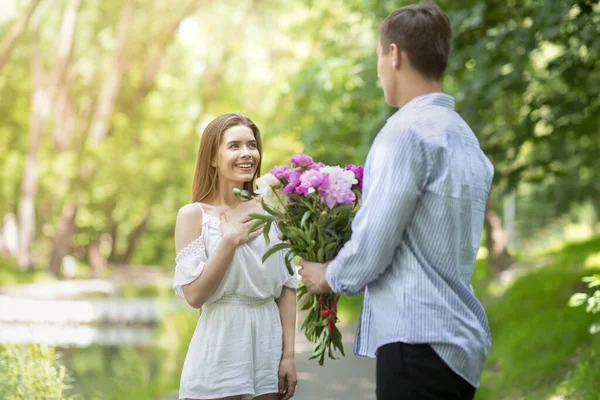 Joven cariñoso sorprendiendo a su novia con ramo de flores en el parque — Foto de Stock