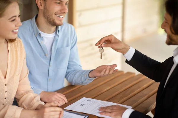 Realtor remettre les clés de la nouvelle maison à couple marié heureux à la table à l'extérieur — Photo