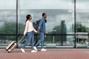 Yolculuk için hazır. Havaalanı yakınlarında bavullarıyla yürüyen mutlu siyah çift.