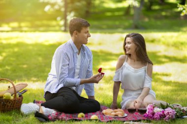 Genç adam kız arkadaşına evlenme teklif ediyor, ona parkta nişan yüzüğü veriyor.