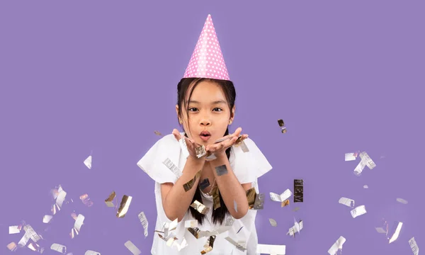 Niña soplando Confetti de plata celebrando cumpleaños sobre fondo púrpura —  Fotos de Stock