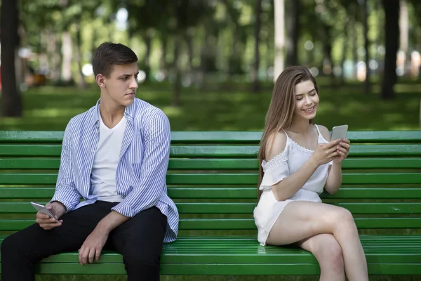 Boring date. Lovely girl chatting on phone and ignoring her boyfriend at park — Stock Photo, Image