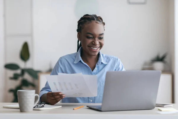 Papeleo. Alegre negro millennial mujer de negocios que trabaja con el ordenador portátil y documentos en la oficina —  Fotos de Stock