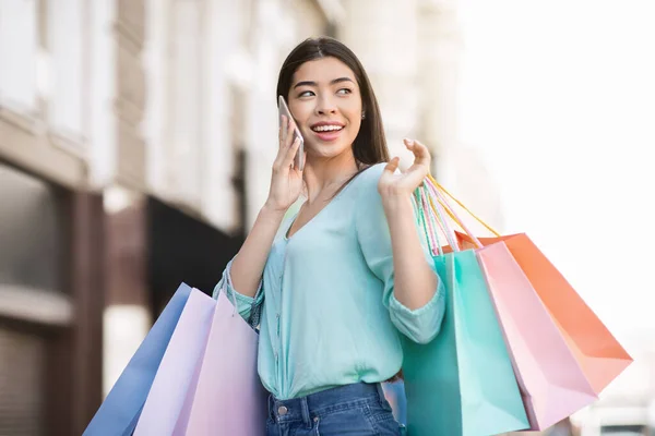 Glad asiatisk flicka promenader med massor av shoppingväskor och prata på mobilen — Stockfoto