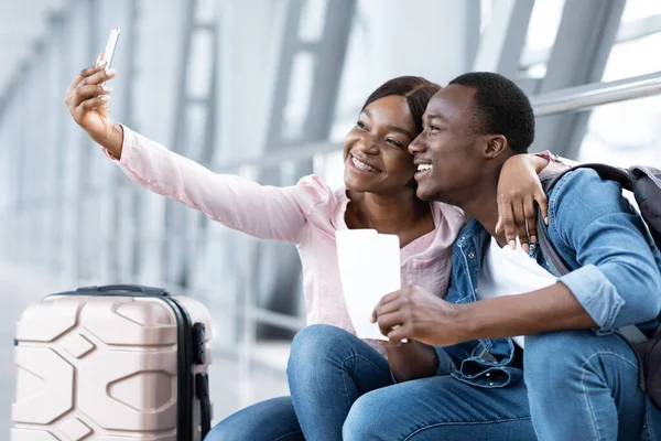Recuerdos de viaje. alegre negro pareja tomando selfie en smartphone en aeropuerto — Foto de Stock