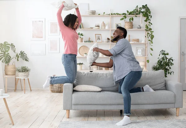 Unga makar fritid. Lekfullt svart par som har kuddkrig i vardagsrummet — Stockfoto