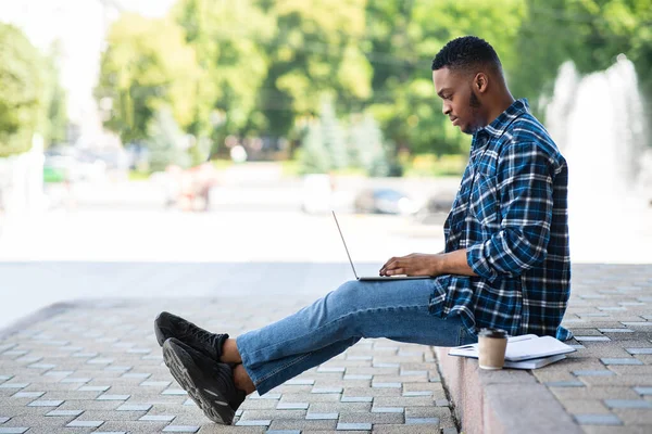 Μαθητής που χρησιμοποιεί φορητό υπολογιστή, κάθεται στα σύνορα στο πάρκο — Φωτογραφία Αρχείου