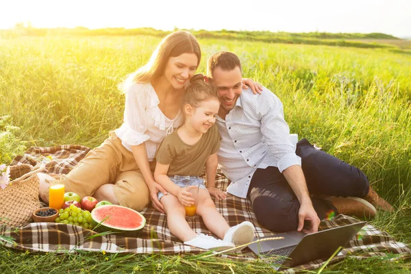 Lycklig familj tillsammans på picknick med dator — Stockfoto