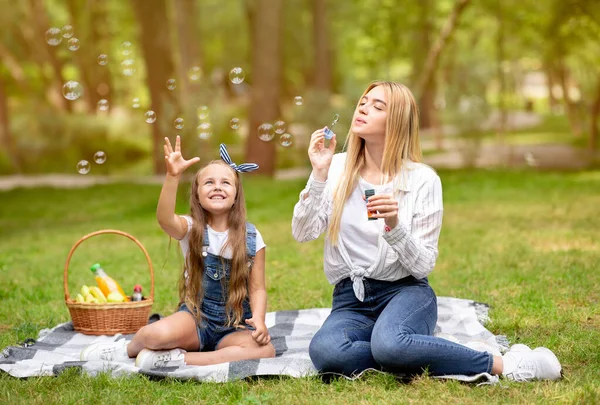 Mamma och dotter blåser såpbubblor ha picknick utomhus — Stockfoto