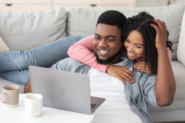 Genç siyah çift evde dizüstü bilgisayarla rahatlıyor, film seyrediyor.