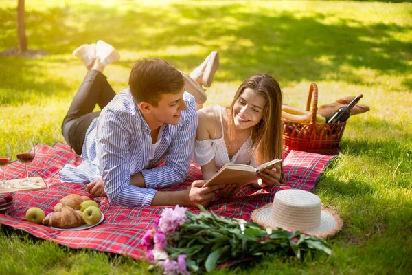 Hermosa pareja casada leyendo libro mientras está acostado en la manta de picnic en el parque —  Fotos de Stock