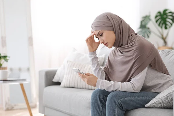 Muchacha árabe molesta en Hijab mirando la pantalla del teléfono inteligente en casa — Foto de Stock