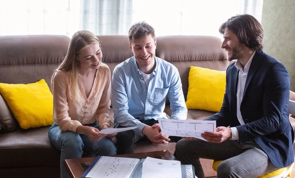 Happy couple with property manager looking at house plan indoors — Stock Photo, Image