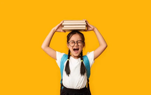 Nespokojená japonská dívka křičící drží knihy na hlavě, žluté pozadí — Stock fotografie
