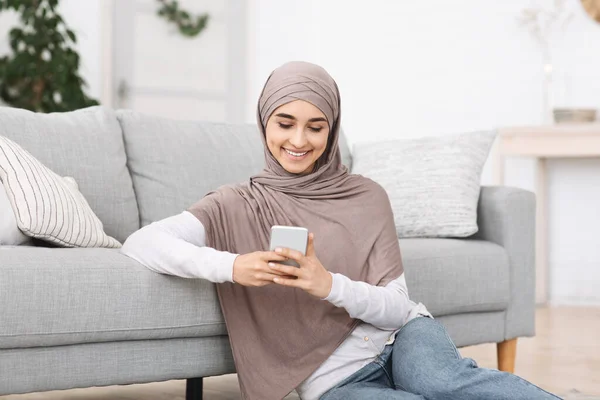 Gadis muslim modern santai di lantai dengan smartphone-nya, pesan dengan teman-teman — Stok Foto