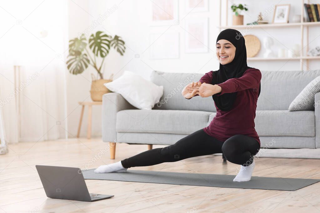 Happy arabic woman doing lunges in front of laptop at home