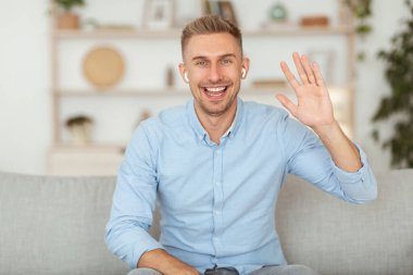 Adam evinde kanepede dinleniyor ve el sallıyor.