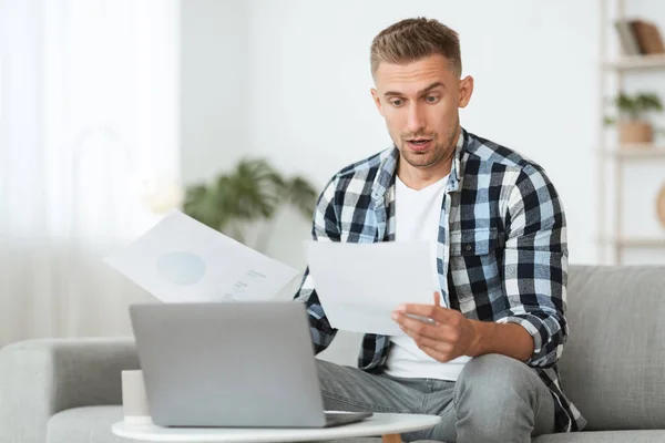 Aufgeregter junger Mann sitzt am Schreibtisch und betrachtet Dokumente — Stockfoto