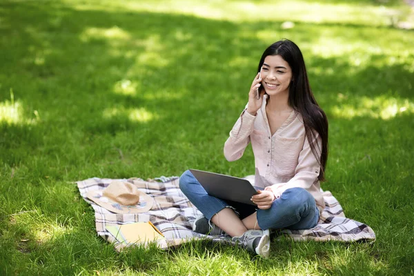 Посміхаючись Азіатська Дівчина Talking На Телефон В той час як Віддалена Робота На відкритому повітрі З Ноутбуком — стокове фото