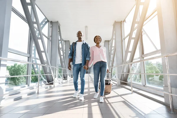 Viajando juntos. Pareja Millennial Africana feliz caminando en el corredor del aeropuerto con maletas — Foto de Stock