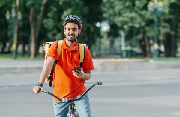 Cyklista s dodávkou. Happy kurýr s batohem, chytré hodinky a smartphone, sedí na kole — Stock fotografie