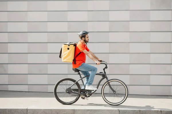 Kurýrní cyklista na šedém pozadí zdi. Mladý muž v helmě s batohem vyjížďky na silnici — Stock fotografie
