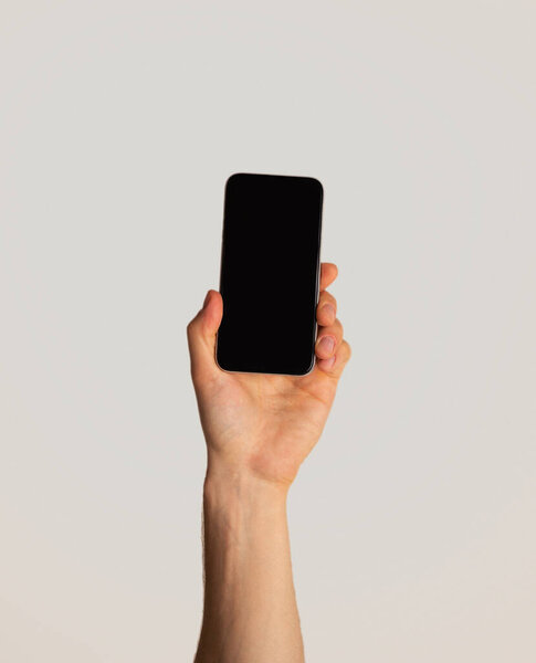 Male hand showing smartphone with empty screen on light background, mockup for mobile app design