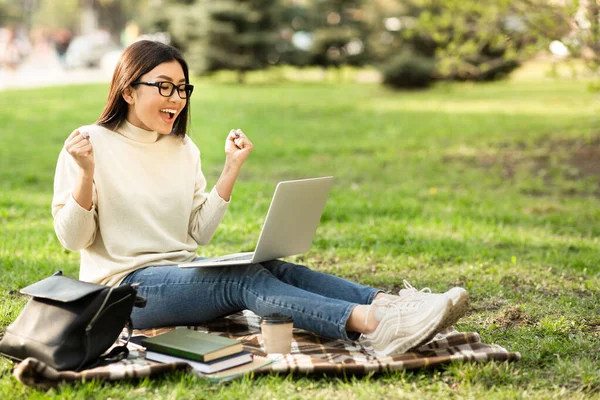 Eccitato asiatico femmina studente lettura buona notizia seduta a parco — Foto Stock