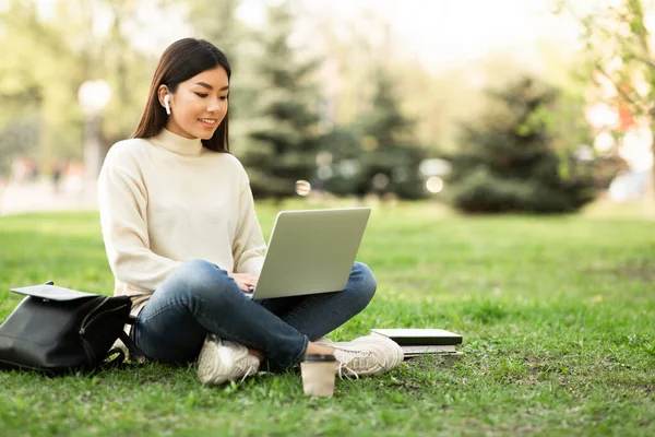 Azji kobieta za pomocą laptopa, siedzi w parku — Zdjęcie stockowe