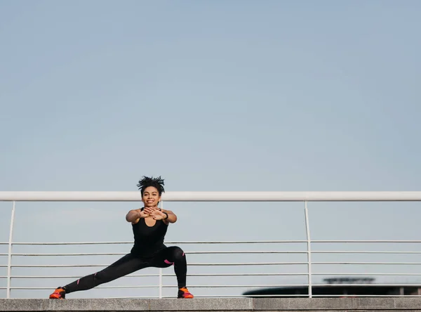 女人锻炼是为了健康.穿着运动服的快乐的非洲裔美国年轻女子，与健美追踪者一起做腿部运动 — 图库照片