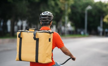 Kasabada kurye var. Kasklı teslimatçı yolda bisiklet sürüyor.