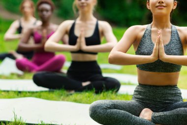 Bir grup sportif kız lotus yogası pozunda meditasyon yapıyor, namaste jestleri yapıyor, yakın çekim yapıyorlar. Boş alan