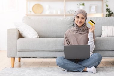 Başörtülü Arap Kadın, bilet rezervasyonu için dizüstü bilgisayar ve kredi kartı kullanıyor