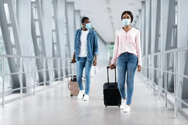 Viajes pandémicos. Gente negra con máscaras caminando con equipaje en la terminal del aeropuerto —  Fotos de Stock