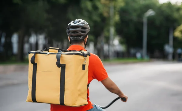 Koerier in de stad. Leverancier in helm met tas rijdt een fiets op de weg — Stockfoto