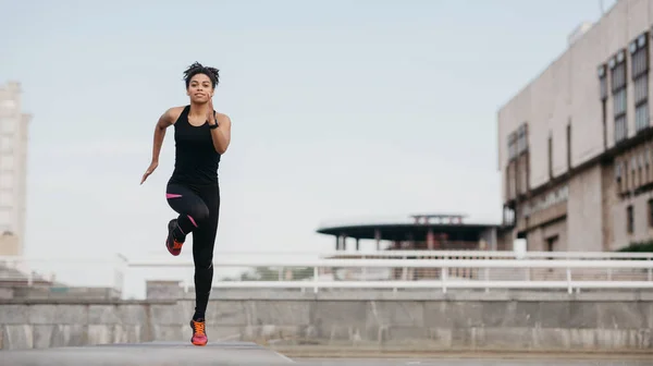 Sportiva per strada. Felice ragazza africana americana in abbigliamento sportivo con fitness tracker corsa veloce — Foto Stock