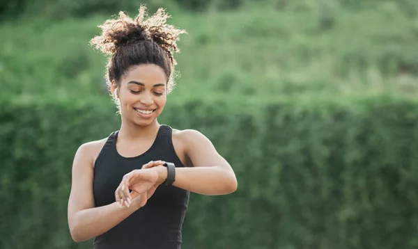 Vitality, sport and results. Glad of result of training, african american girl with headphones checking fitness tracker — Stock Photo, Image